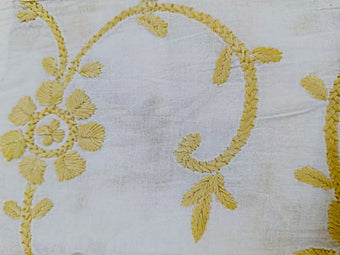Close-up of yellow Ulti bakhiya chikankari  embroidery on white fabric