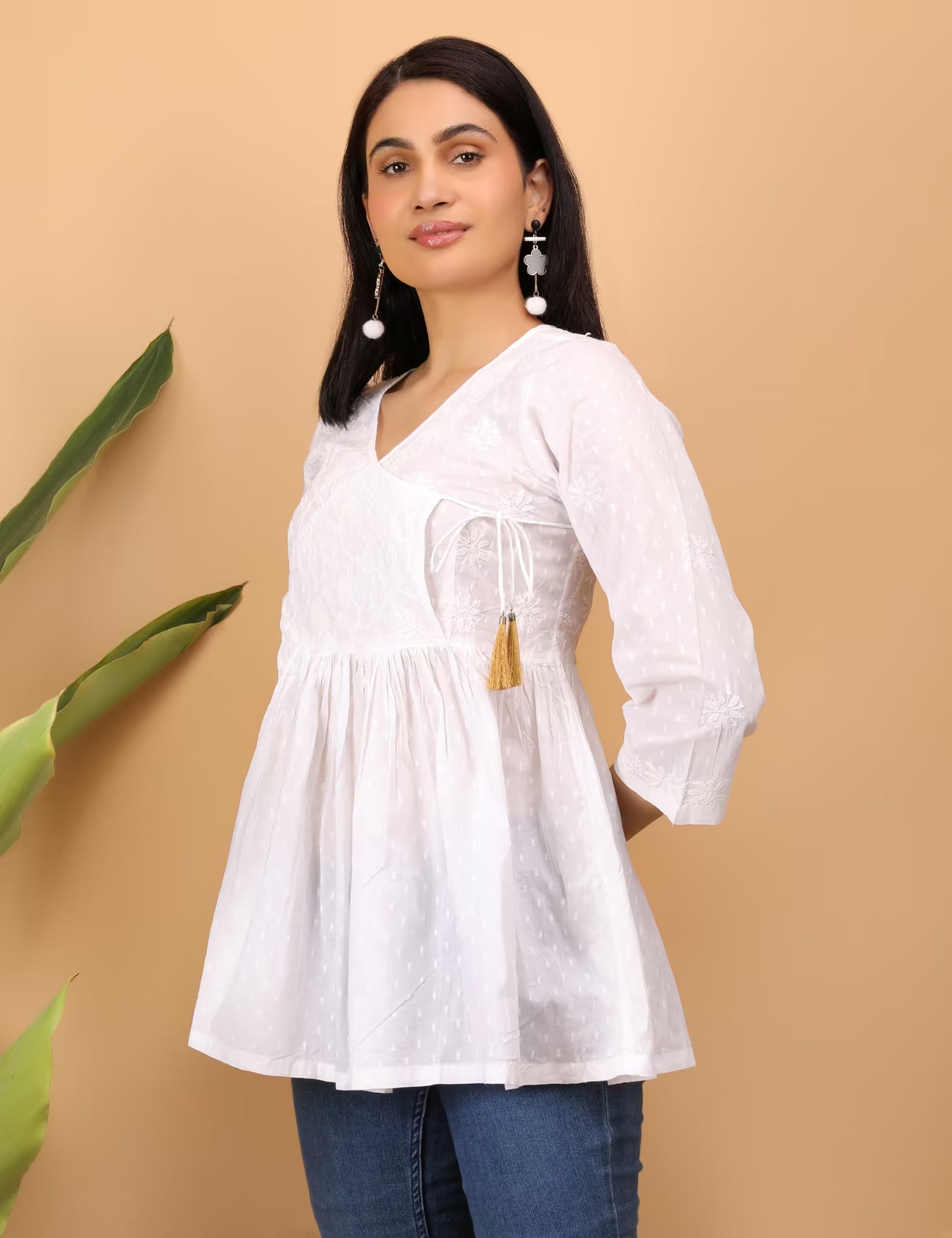 Woman wearing a white chikankari top with tassels on a beige background