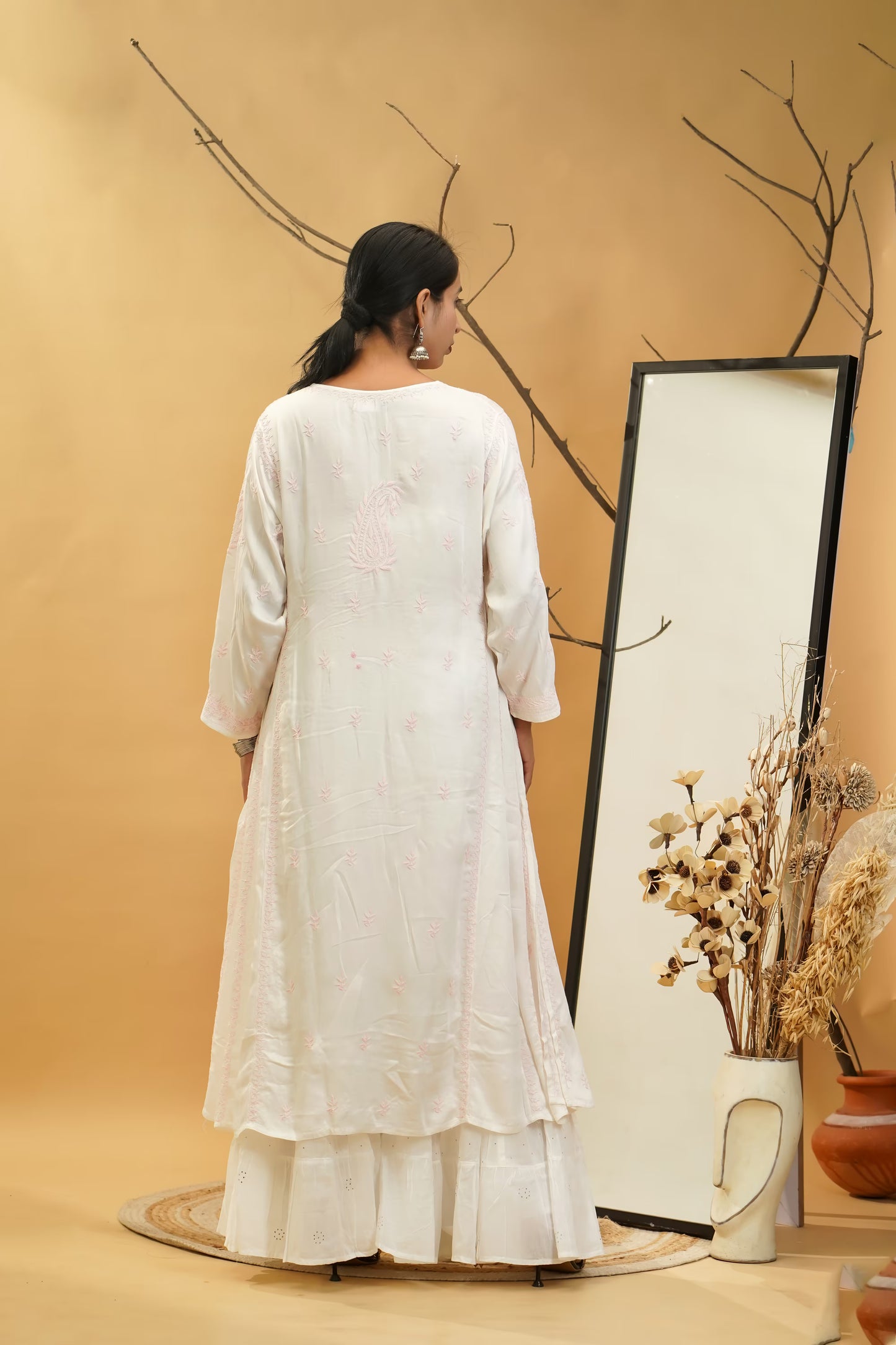 Woman in a white dress standing in front of a mirror with a beige background