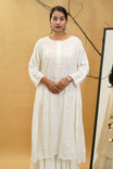 Woman wearing a white traditional outfit against a beige background