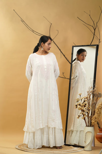 Woman in a white dress standing next to a mirror on a beige background