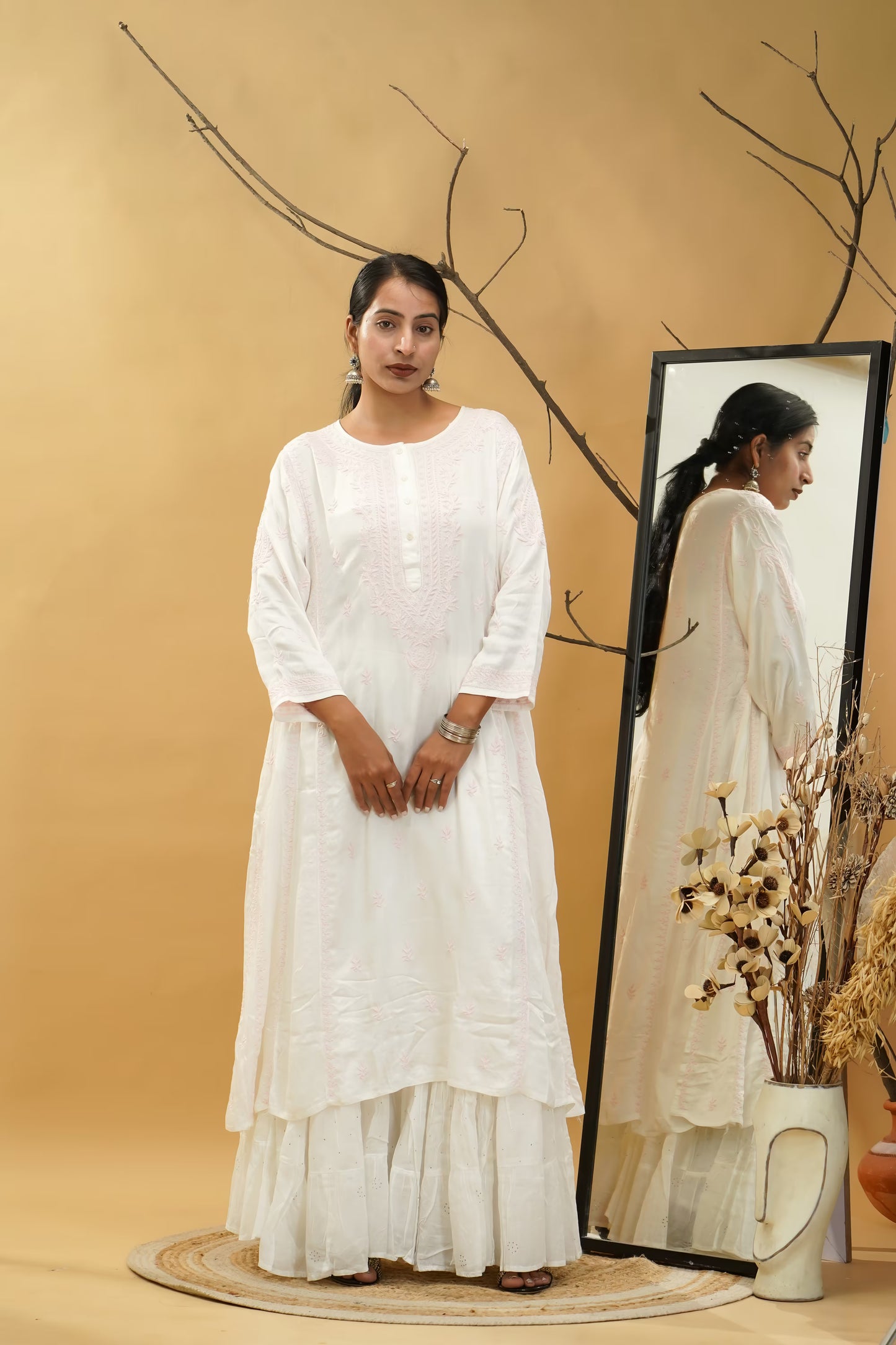Woman in a white dress standing next to a mirror with a beige background