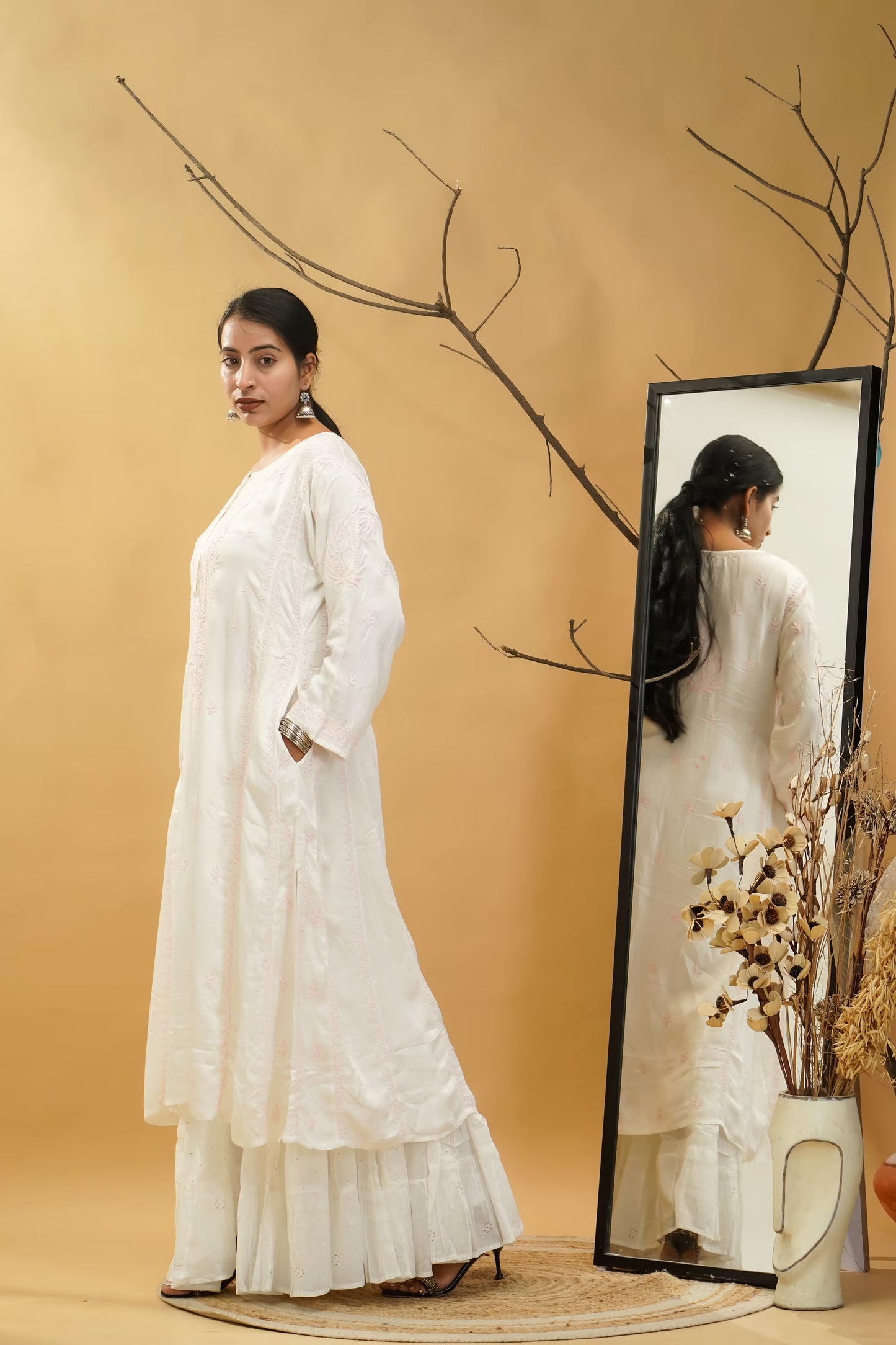 Woman in a white dress standing next to a mirror on a beige background