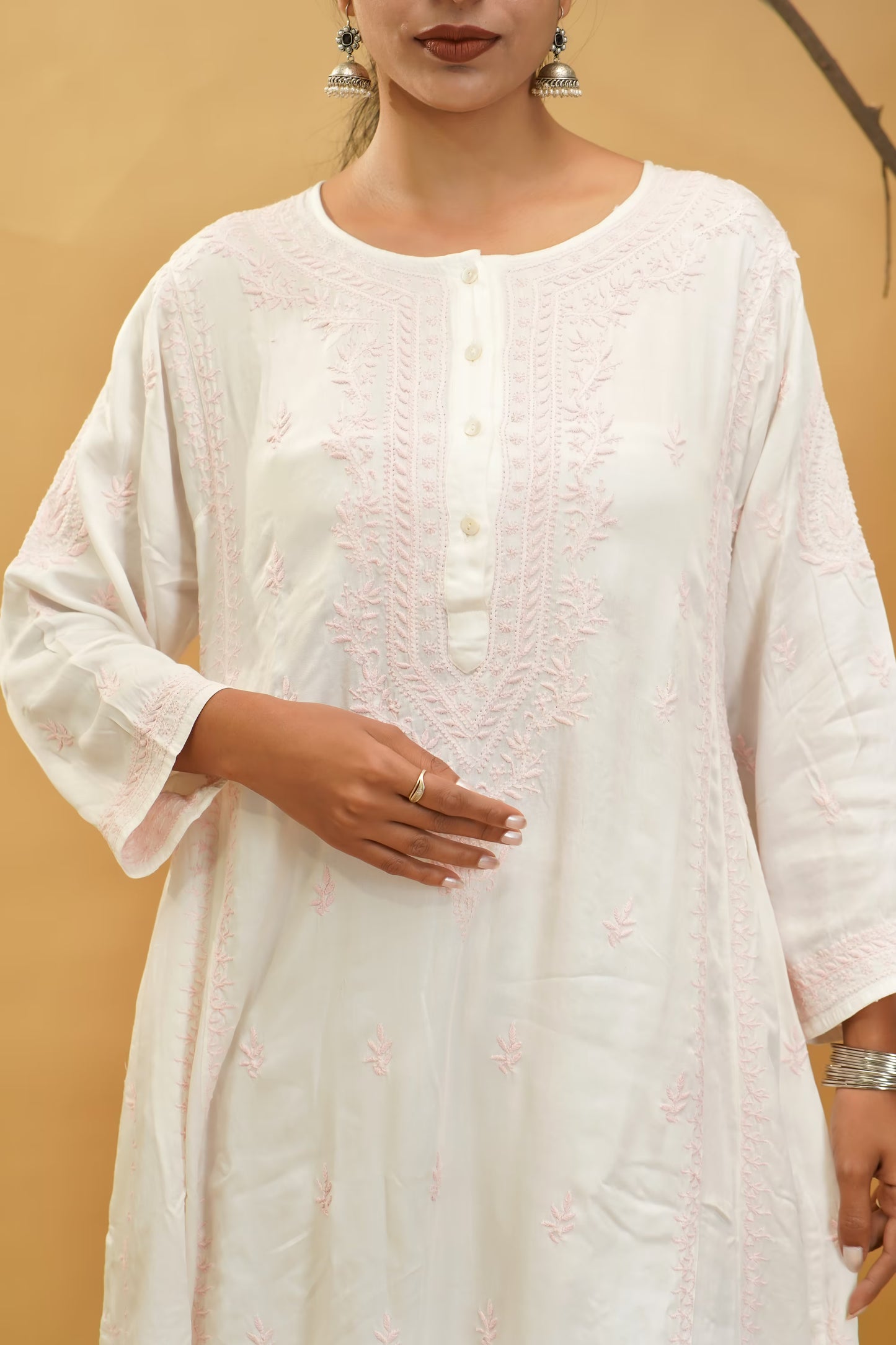Woman wearing a light pink embroidered kurta against a beige background
