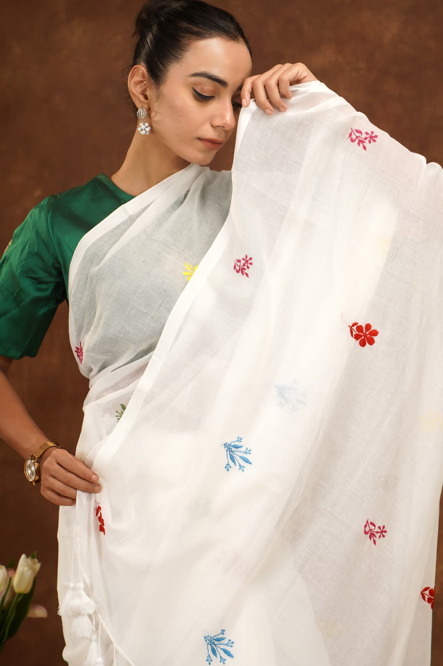 Woman holding a white saree with colorful floral patterns against a brown background