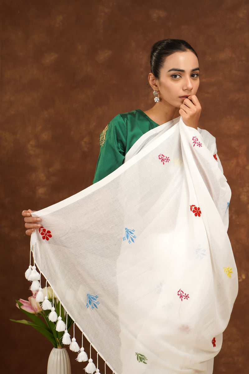 Woman wearing a white saree with colorful patterns against a brown background