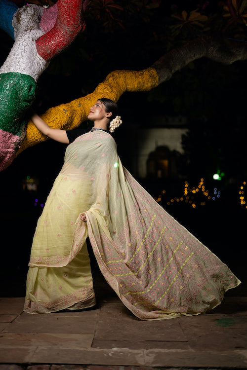 Woman in a traditional outfit standing against a colorful wall at night.