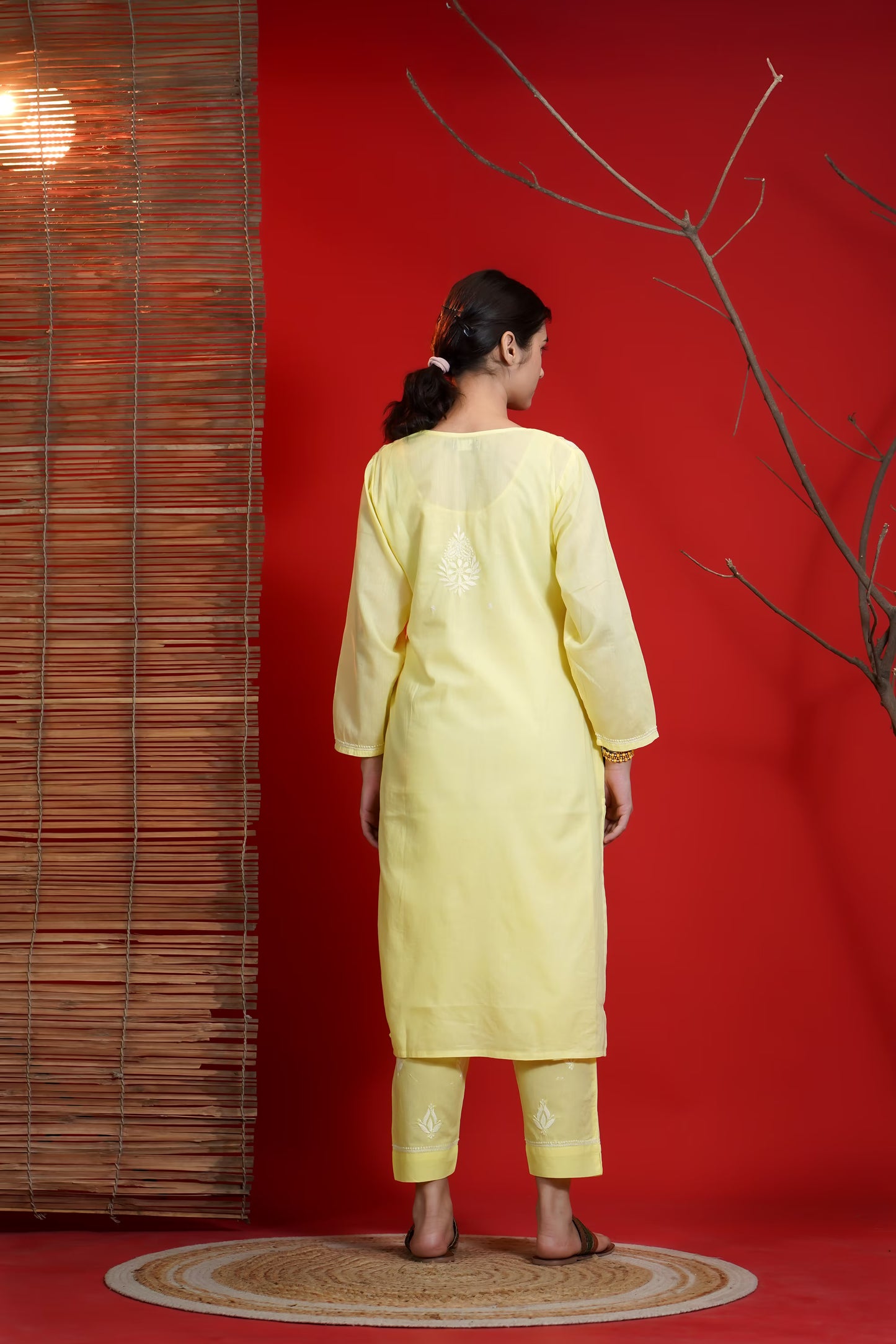 Woman in a yellow traditional outfit standing against a red wall with a wooden panel.