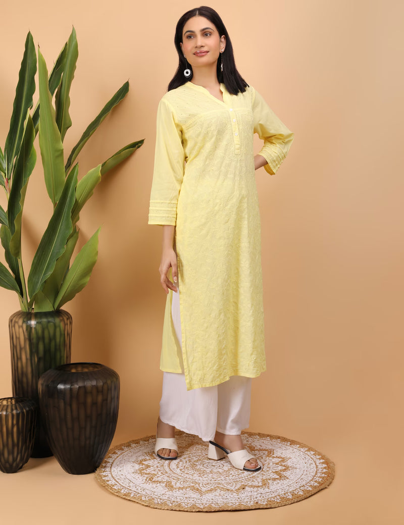 Woman wearing a yellow kurta with white pants standing against a beige background