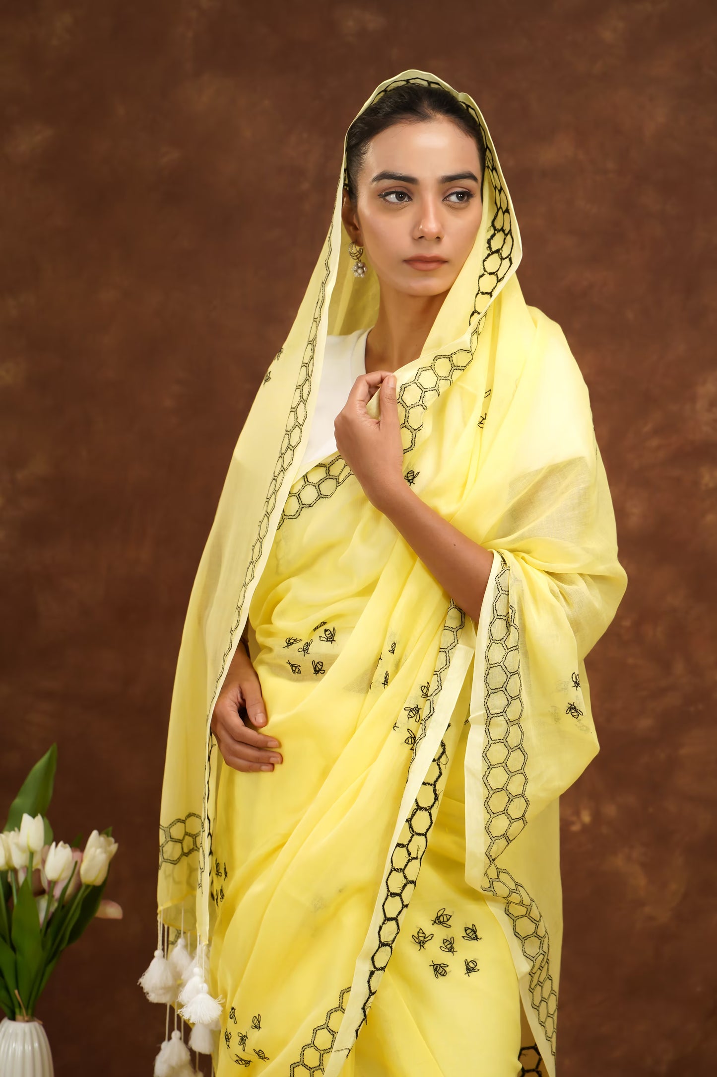 Woman wearing a yellow saree with black patterns against a brown background
