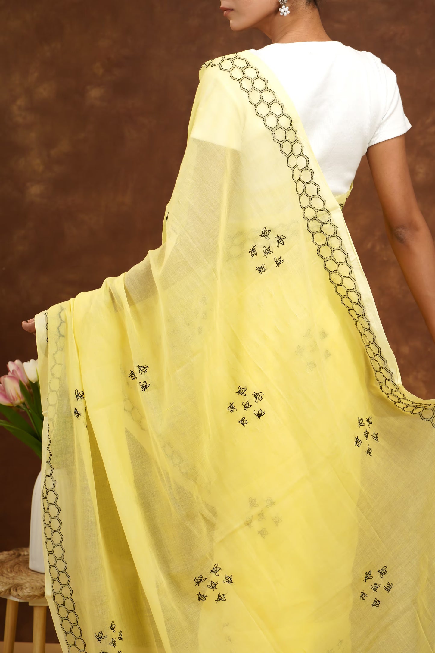 Woman wearing a yellow saree with black patterns and a white blouse against a brown background