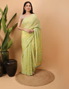 Woman in a yellow  Chikankari saree standing against a beige background with decorative elements.