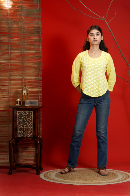 Woman in yellow top and blue jeans standing against a red wall with a wooden side table.