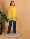 Woman wearing a yellow scarf and blue pants standing against a beige background
