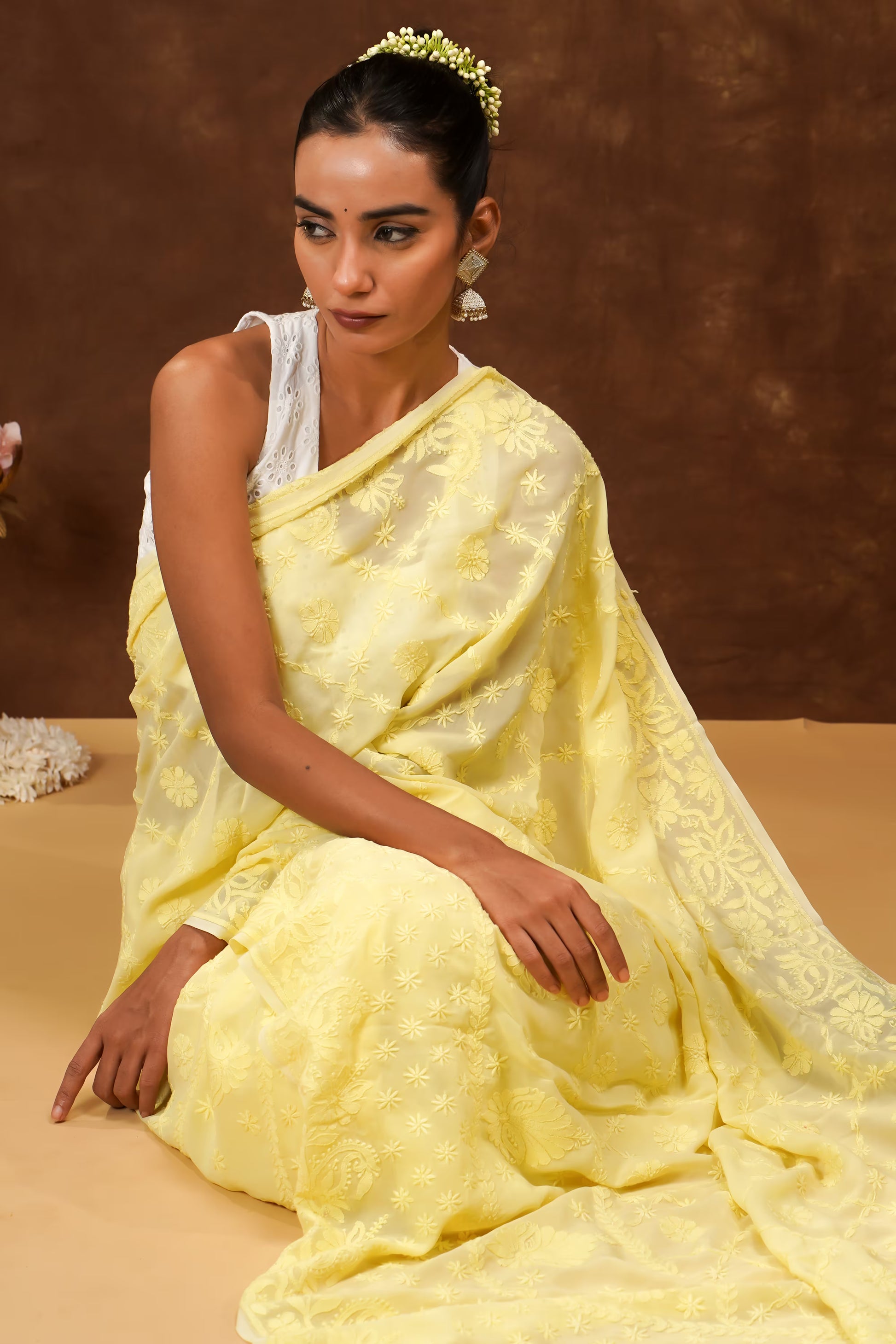 Woman in a yellow saree sitting on a brown background