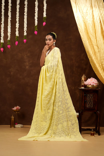 Woman in a yellow saree standing in a decorated room with flowers and a curtain.