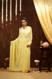 Woman in a yellow saree standing in a decorated room with flowers and lights.