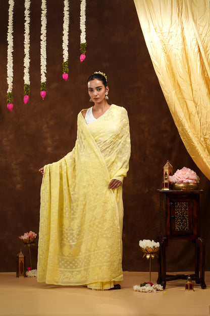 Woman in a yellow saree standing in a decorated room with flowers and lights.