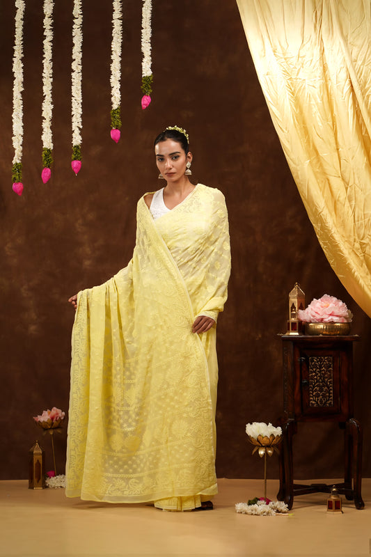 Woman in a yellow saree standing in a decorated room with flowers and lights.