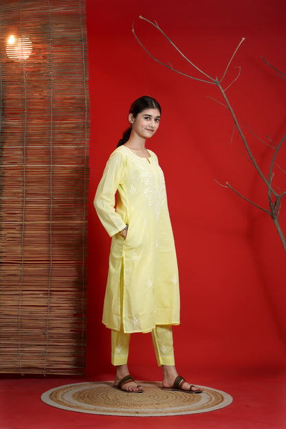 Woman in a yellow outfit standing against a red wall with a wooden panel and branch decor.